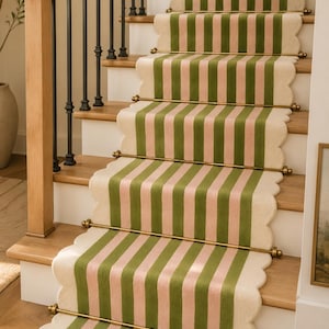 May include: A staircase runner featuring vertical stripes in alternating shades of sage green and soft pink, finished with a scalloped edge. The runner is secured to the wooden stair treads with polished brass rods and finials at each step.