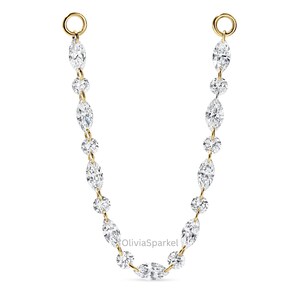 May include: A gold chain connector featuring alternating marquise-cut and round-cut clear stones arranged in a U-shape. The piece includes two circular gold jump rings at the top ends for attachment. The text OliviaSparkel is visible in the centre.