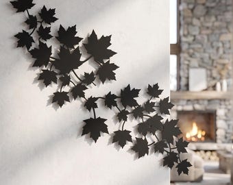 May include: A matte black metal wall art piece featuring a sprawling branch design adorned with numerous maple leaves. The silhouette is mounted on a light-colored wall, creating a sharp contrast with the dark, intricate foliage pattern.