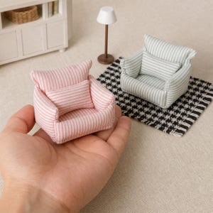 Op de afbeelding: Twee miniatuurfauteuils met een wit en pastelkleurig gestreepte stoffen bekleding, elk voorzien van een bijpassend rechthoekig sierkussen. De ene stoel is roze-wit, de andere groen-wit, ontworpen voor presentaties op poppenhuisschaal.