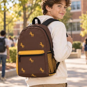 May include: A brown backpack featuring a repeating pattern of small yellow horse silhouettes. The bag includes a front zippered pocket with a yellow trim, black shoulder straps, and a yellow mesh side pocket for storage, all constructed from fabric.
