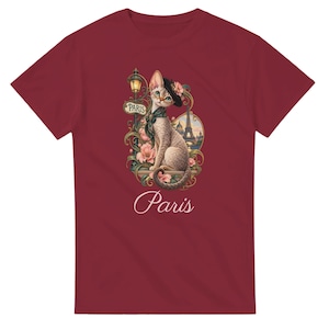 Peut inclure: Un t-shirt à manches courtes bordeaux avec une illustration de chat portant un béret noir et une écharpe verte. Le chat est assis près d'un réverbère, de fleurs roses et de la tour Eiffel. Le mot "PARIS" est écrit sur un panneau et en dessous.