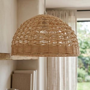 May include: A dome-shaped pendant light fixture crafted from natural light brown woven rattan. The shade features an open lattice pattern on the upper section and a tightly woven band along the bottom edge, suspended by a simple white cord.