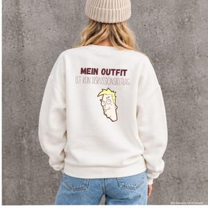 Könnte beinhalten: Ein cremefarbenes Langarm-Sweatshirt mit dem Text MEIN OUTFIT IST KEIN DISKUSSIONSBEITRAG in Dunkelrot und Schwarz, ergänzt durch eine Cartoon-Illustration eines Kopfes mit blonden Haaren und einem neutralen Gesichtsausdruck.