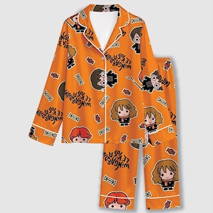 May include: A long-sleeved button-down pajama shirt and matching pants in bright orange, featuring a repeating pattern of cartoon characters, candies, and the text Wingardium Leviosa in black, with white piping along the collar and cuffs.
