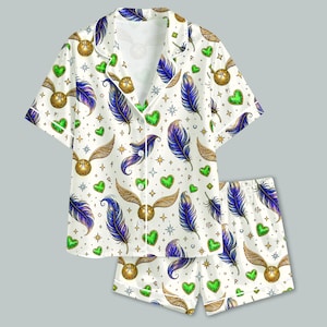 May include: A short-sleeved button-down pajama shirt and matching shorts set in white, featuring a repeating pattern of gold winged spheres, blue and purple feathers, green hearts, and small stars scattered across the fabric surface.