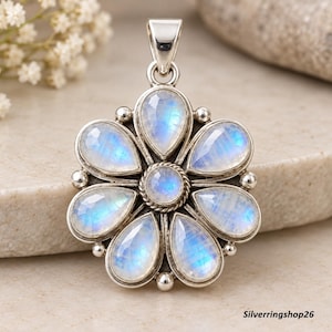 May include: A silver pendant shaped like a flower with seven pear-shaped faceted moonstones surrounding a central round moonstone. The stones exhibit a blue adularescence. The metal setting features a twisted rope border and small silver spheres.
