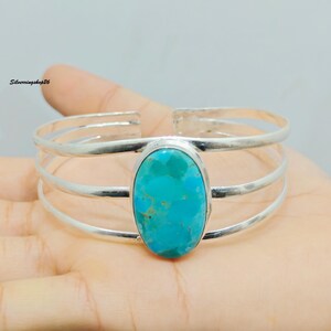 Könnte beinhalten: Ein Silberarmreif mit einem zentralen, ovalen Türkis-Edelstein mit natürlicher Maserung. Das Armband besteht aus drei parallelen Silberdrähten, die an der Fassung zusammenlaufen. Der Text Silverringshop26 ist in der Ecke zu sehen.