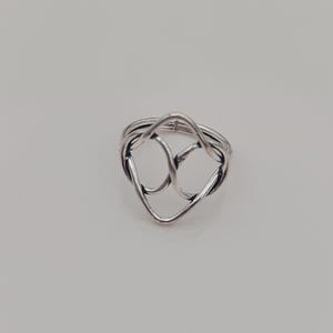 May include: A silver-toned ring featuring an open, abstract design composed of interconnected, flowing wire-like loops. The metal has a polished finish with darkened recessed areas that emphasize the continuous, intertwined shape of the band.
