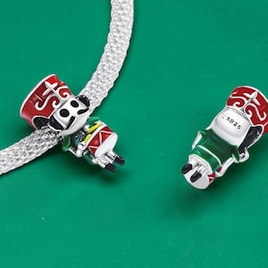 Peut inclure: Deux perles breloques en argent en forme de soldats jouets, avec des détails en émail rouge et vert. Une breloque est enfilée sur une chaîne serpent en argent, tandis que l'autre est posée à côté, montrant le poinçon S925 au dos.