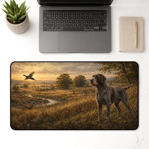 May include: A rectangular desk mat featuring a detailed landscape illustration of a brown and white wirehaired pointing dog standing in a grassy field at sunset, with a pheasant flying in the distance and another pheasant near a small stream.