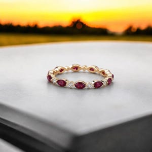Könnte beinhalten: Ein Goldring mit einem abwechselnden Muster aus marquise-geschliffenen roten Rubinen und kleinen rund geschliffenen weißen Diamanten. Die Edelsteine sind in einer durchgehenden Reihe um den Ringumfang gefasst und bilden ein symmetrisches Design.