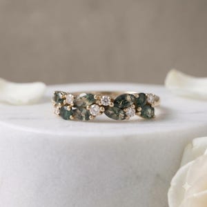 Könnte beinhalten: Ein Goldring mit einer Anordnung aus marquise-geschliffenen Moosachat-Steinen mit dunkelgrünen Einschlüssen und kleinen runden weißen Diamanten. Die Steine sind in einem horizontalen Band angeordnet und wechseln sich ab zwischen grünem Achat und klaren Diamanten.