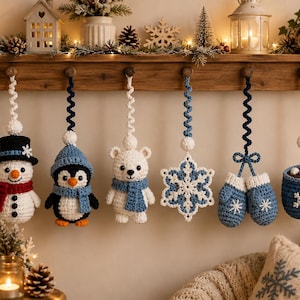 May include: Six crocheted Christmas ornaments hanging from a wooden shelf. The set includes a snowman with a top hat, a penguin, a polar bear, a snowflake, a pair of blue mittens, and a mug of hot cocoa with a candy cane, all in winter colors.