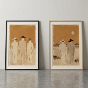 May include: Two framed wall art prints featuring painted figures in hats. The left print shows three figures in light suits and dark hats against a tan background. The right print shows two figures in light suits and hats looking toward a horizon with a sun.