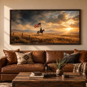 May include: A rectangular framed wall art print depicting a lone rider on horseback carrying an American flag across a vast, golden prairie landscape under a dramatic, cloudy sunset sky, mounted above a brown leather sofa in a living room.