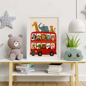 May include: A framed art print featuring a bright red double-decker bus filled with various illustrated animals, including a giraffe, elephant, lion, zebra, and monkey, displayed in a white frame on a wooden table with books and toys.