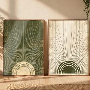 May include: Two rectangular framed wall art prints featuring a sunburst design. The left print has a dark green background with a cream-colored semi-circle. The right print has a cream background with a dark green semi-circle.