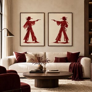 May include: Two framed wall art prints featuring identical illustrations of a figure in a wide-brimmed hat, long-sleeved top, and wide-leg trousers, holding a pistol in a red ink sketch style against a cream-colored background.