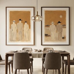 May include: Two framed wall art prints featuring abstract figures in hats against a warm ochre background. The left print shows three figures, while the right print depicts two figures in a landscape. Both are displayed in dark wood frames.