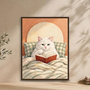 Bookish wall art print of a fluffy white cat with green eyes reading a book in bed, framed and leaning against a warm terracotta wall — funny cat wall art for book lovers