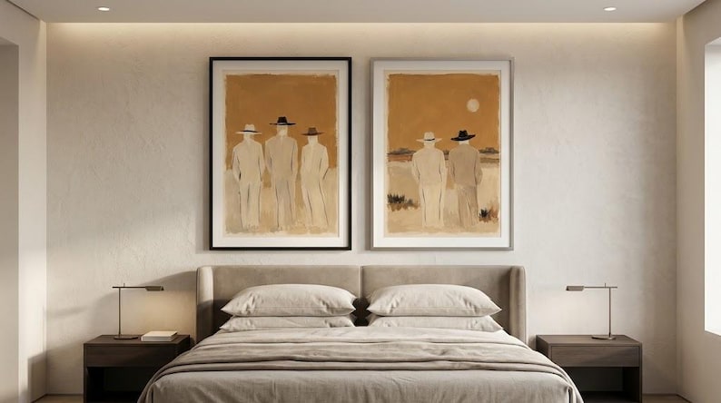 May include: Two framed wall art prints featuring abstract figures in hats against a warm, tan-coloured background. The left print shows three figures standing, while the right print depicts two figures facing a horizon with a pale sun in the sky.