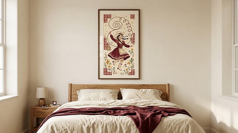 Dancing cowgirl folk art print above a bed with a wooden headboard and burgundy throw — cowgirl bedroom wall art, digital download