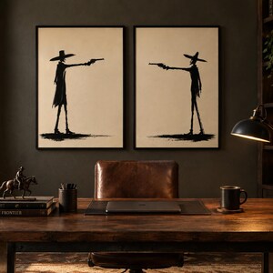 Pu&ograve; includere: Due stampe da parete incorniciate con illustrazioni a silhouette nera di figure con cappelli a tesa larga che puntano revolver l'una contro l'altra, su sfondo beige chiaro, esposte fianco a fianco su una parete scura sopra una scrivania.