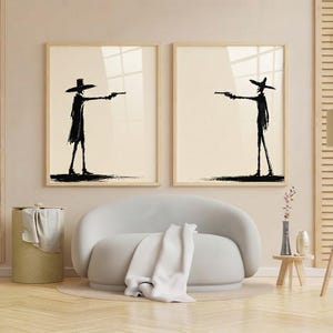 Pu&ograve; includere: Due stampe da parete incorniciate con sagome a inchiostro nero di figure che indossano cappelli a tesa larga e impugnano pistole. Le figure sono raffigurate in uno scontro, l'una di fronte all'altra, su uno sfondo beige chiaro.