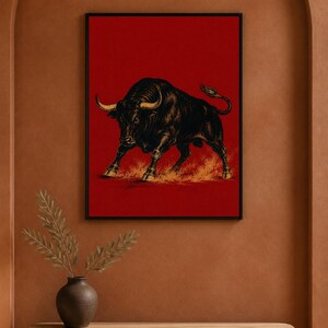 May include: A framed wall art print featuring a detailed black illustration of a charging bull with golden horns and hooves, set against a solid red background. The bull is depicted in a dynamic stance with dust kicking up beneath its feet.