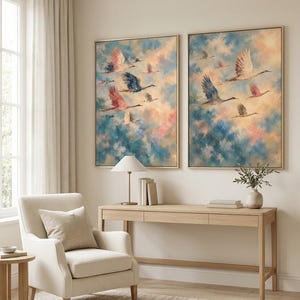 May include: Two framed rectangular wall art prints featuring a flock of birds in flight against a soft, painterly sky of blended blue, pink, and cream tones. The artwork is displayed side-by-side on a wall above a light wood console table.