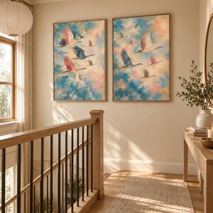 May include: Two rectangular wall art prints featuring a flock of birds in flight against a textured sky of blue, pink, and cream clouds. Each print is encased in a thin, light-toned wooden frame, displaying a soft, painterly aesthetic.