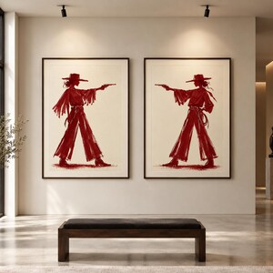 May include: Two framed wall art prints featuring a deep red illustration of a person wearing a wide-brimmed hat, a long-sleeved shirt with fringe, and wide-leg trousers, holding a pistol in an outstretched arm, set against a light background.