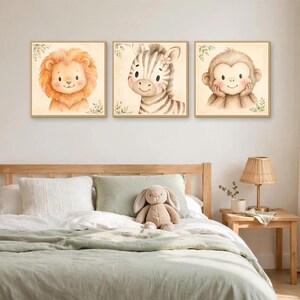 K&ouml;nnte beinhalten: Ein Set aus drei quadratischen Wandbildern mit Aquarellillustrationen eines L&ouml;wen, eines Zebras und eines Affen. Jedes Tier ist mit weichen Z&uuml;gen, rosigen Wangen und kleinen gr&uuml;nen Blattakzenten auf beigem Hintergrund dargestellt.