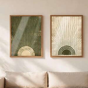 May include: Two framed wall art prints featuring a sunburst motif. The left print has a dark olive green background with a cream sun, while the right print has a cream background with an olive green sun. Both feature thin radiating lines.