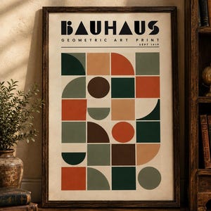 K&ouml;nnte beinhalten: Ein gerahmter Kunstdruck mit der Aufschrift BAUHAUS GEOMETRIC ART PRINT SEPT 1919. Das Poster zeigt ein Raster aus geometrischen Formen wie Kreisen, Halbkreisen und Quadraten in einer Palette aus Dunkelgr&uuml;n, Rostorange, Braun und Beige.