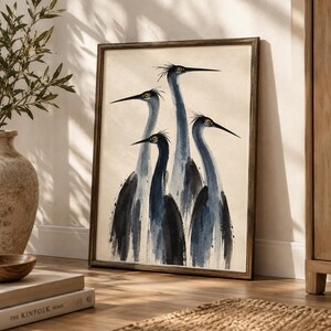 May include: A framed wall art print featuring a watercolour illustration of four long-necked birds with blue and black plumage and yellow eyes. The birds are depicted in a vertical composition against a light beige background within a dark wood frame.
