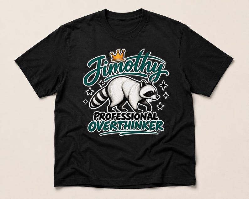 May include: A black short-sleeved t-shirt featuring a graphic of a raccoon wearing a crown. The text reads Jimothy above the raccoon and PROFESSIONAL OVERTHINKER below it, surrounded by small star shapes in a teal and white colour scheme.