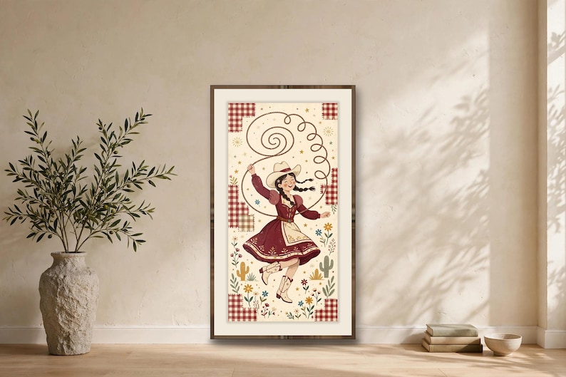 May include: A framed vertical wall art print featuring a person in a cowboy hat and dress spinning a lasso. The illustration includes red gingham patches, small cacti, and colorful flowers on a cream background with a dark wood frame.