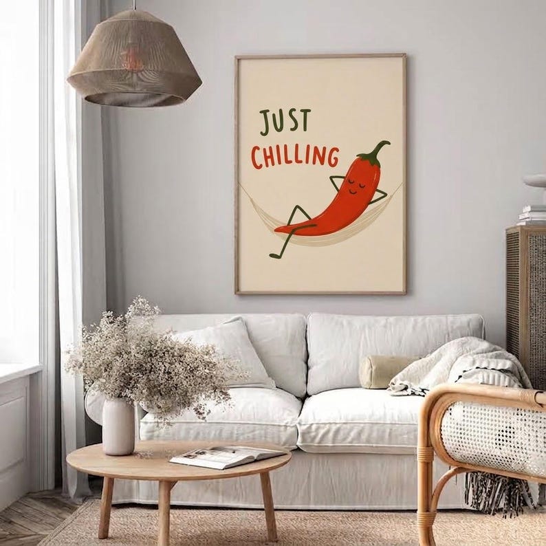 May include: A rectangular wall art print featuring a cartoon red chili pepper with a smiling face relaxing in a hammock. The text "JUST CHILLING" is printed above the chili pepper in dark green and red lettering against a light beige background.