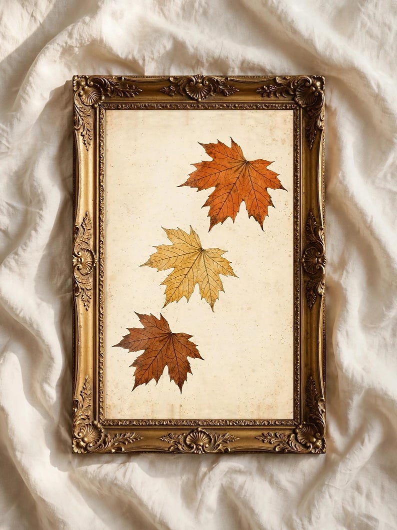 May include: A rectangular wall art piece featuring three pressed maple leaves in shades of orange, yellow, and brown, displayed on a cream-colored background within an ornate, antique-style gold-toned frame with intricate carved detailing.