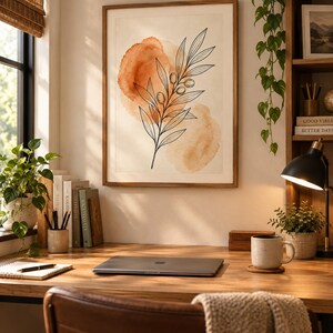May include: A framed wall art print featuring a black line drawing of an olive branch with leaves and small olives, layered over two soft, abstract watercolor shapes in shades of burnt orange and light peach on a cream-colored background.