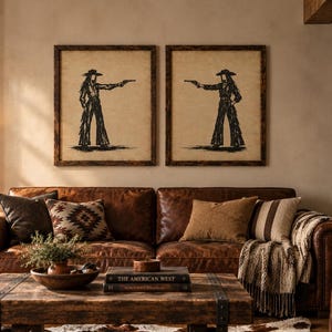 K&ouml;nnte beinhalten: Zwei gerahmte Wandbilder mit schwarzen Tuschezeichnungen von Figuren mit Cowboyh&uuml;ten und Fransenhosen, die Pistolen halten, platziert &uuml;ber einem braunen Ledersofa mit dekorativen Kissen und einem Couchtisch aus Holz in einem Wohnzimmer.