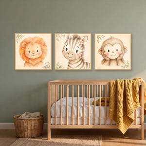 K&ouml;nnte beinhalten: Drei quadratische Wandbilder mit Aquarellillustrationen eines L&ouml;wen, eines Zebras und eines Affen. Jedes Tier ist mit weichen Gesichtsz&uuml;gen, rosigen Wangen und kleinen gr&uuml;nen Blattakzenten auf einem cremefarbenen Hintergrund dargestellt.