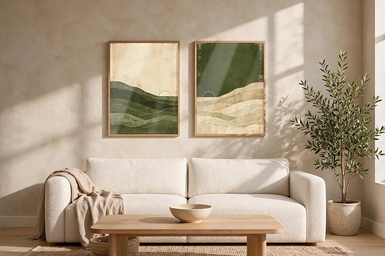 May include: Two framed rectangular wall art prints featuring abstract landscape designs. The left print displays layered green hills against a cream background, while the right print shows a dark green sky over beige rolling hills and a sun icon.