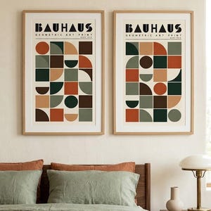 K&ouml;nnte beinhalten: Zwei gerahmte Kunstdrucke mit dem Text BAUHAUS GEOMETRIC ART PRINT. Jeder Druck zeigt ein Raster aus geometrischen Formen wie Kreisen, Halbkreisen und Quadraten in einer Farbpalette aus Dunkelgr&uuml;n, Rostorange, Braun und Beige.