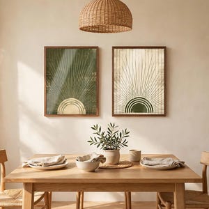 May include: Two rectangular framed wall art prints featuring a sunburst design with radiating lines. The left print has a dark green background with a gold sun, while the right print has a cream background with a dark green sun.