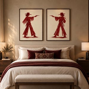 May include: Two framed wall art prints featuring a deep red ink illustration of a figure wearing a wide-brimmed hat and fringed clothing, holding a pistol in an outstretched arm. The figures are depicted in profile, facing toward each other.