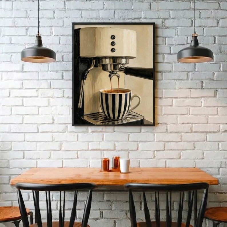 May include: A framed wall art print depicting a cream-colored espresso machine brewing coffee into a black and white striped ceramic mug. The machine features a black portafilter and three circular buttons on the front panel, set against a neutral background.