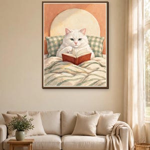 White cat reading in bed art print framed above a sofa in a cozy living room — cute bookish wall art for cat and book lovers